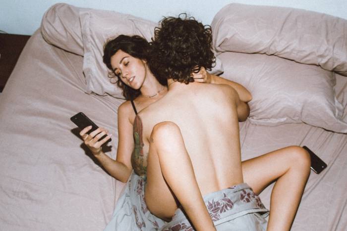 Žena leží v posteli a v ruce má smartphone